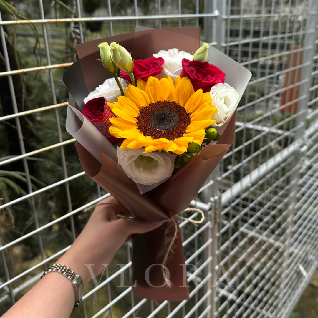 Bouquet of flowers with a sunflower held by a person against a wire fence background