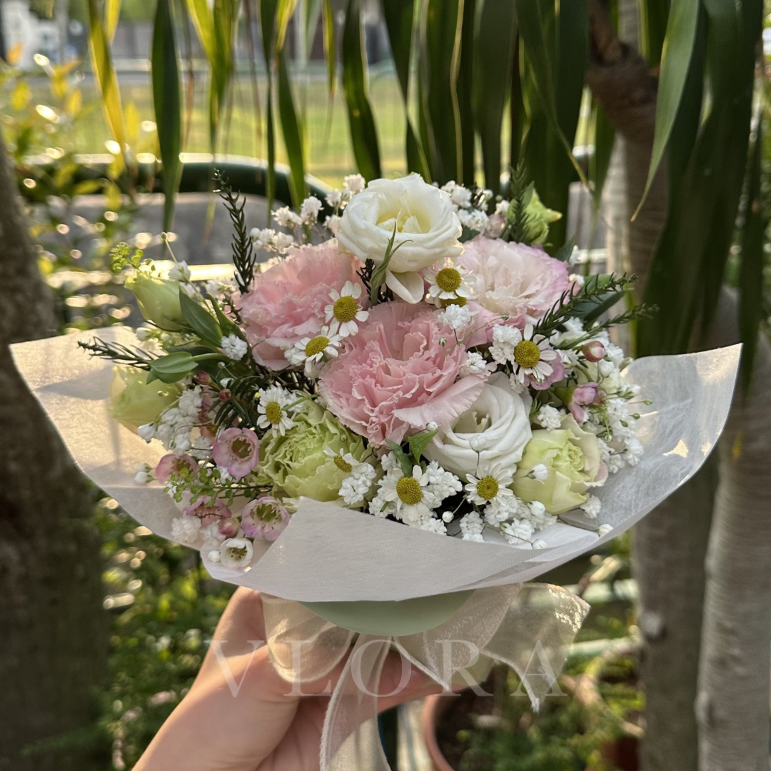 Table arrangement of pink eustoma flowers held by a hand with a blurred green outdoor background