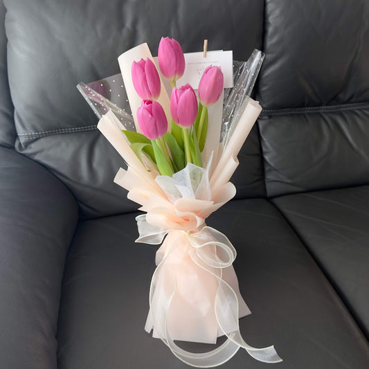 A bouquet of pink tulips arranged elegantly with white and pink wrapping, presented on a dark couch.