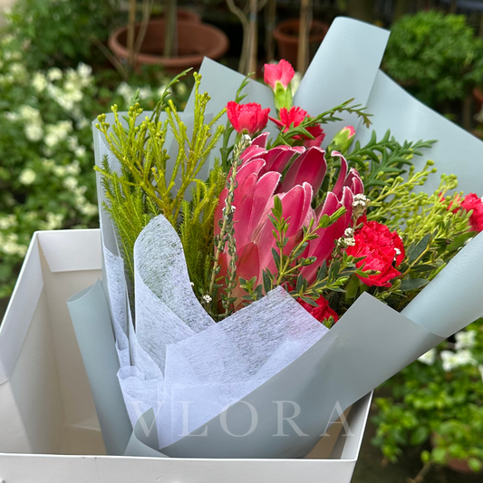 Bouquet of South African protea flowers with greenery in a white box, brand 'VLORA' visible
