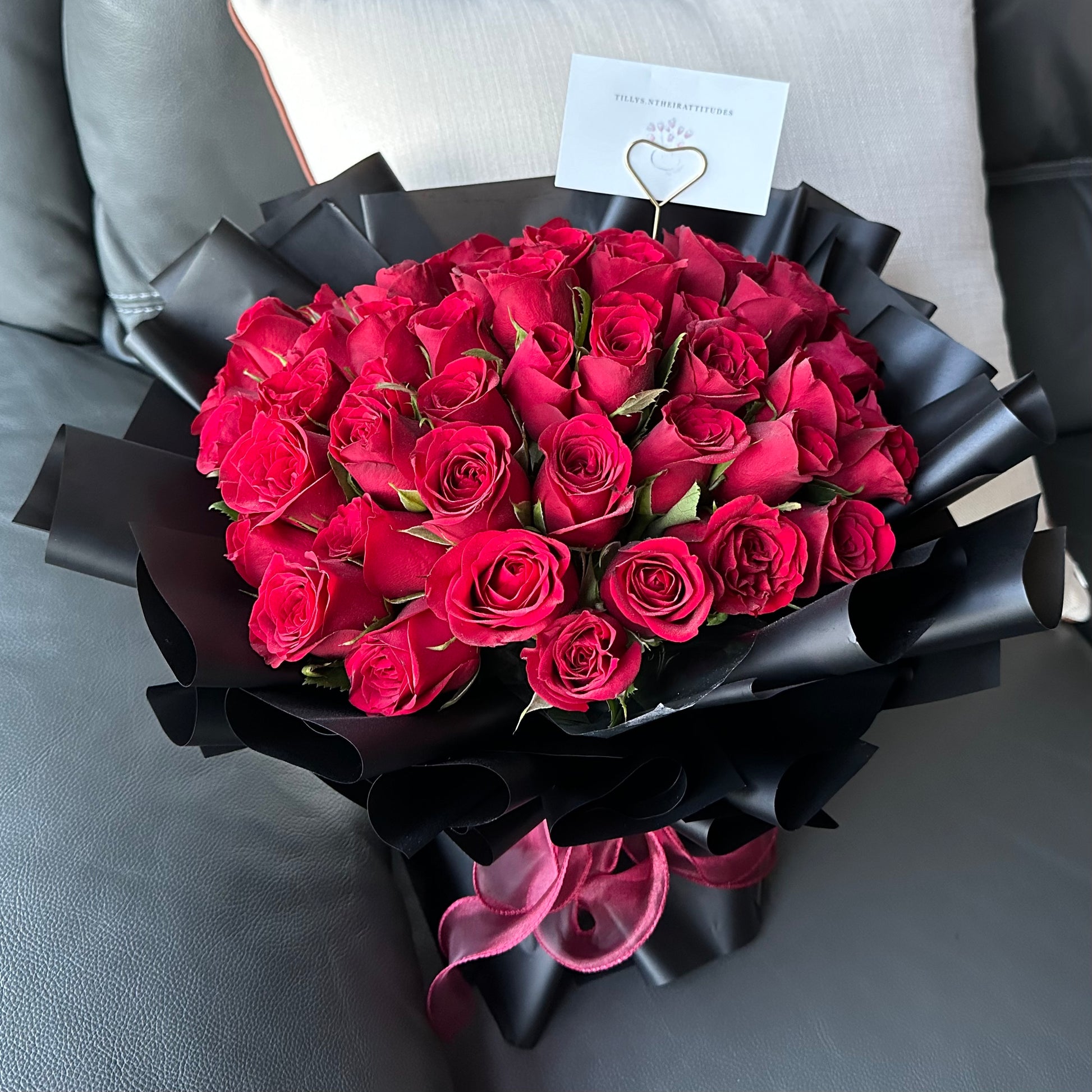 A bouquet of 50 red roses wrapped in black paper with a message card attached.