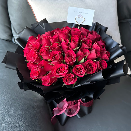 A bouquet of 50 red roses wrapped in black paper with a message card attached.