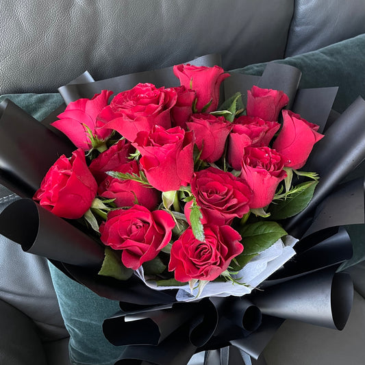 A bouquet of red roses wrapped in black paper.