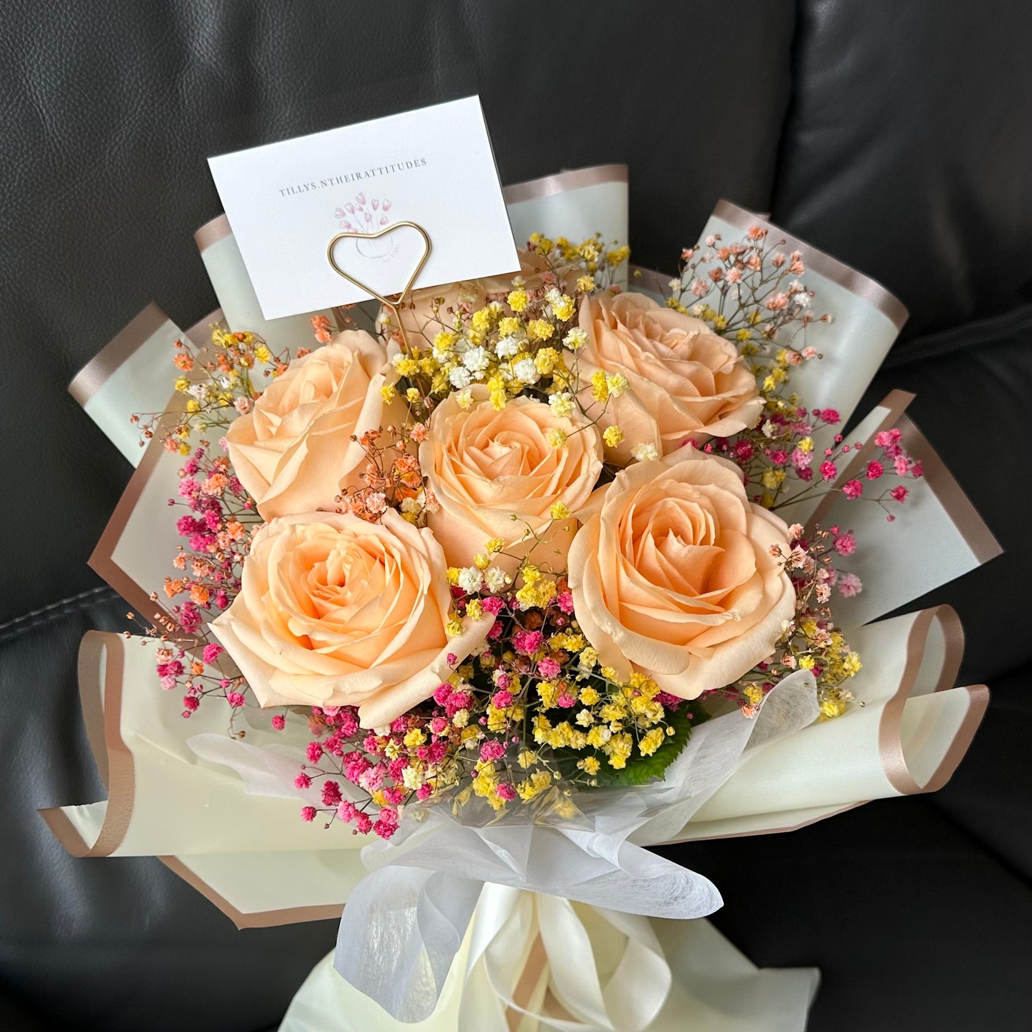 A bouquet of champagne Roses and rainbow Baby’s Breath presented on a dark background, with a complimentary message card included.