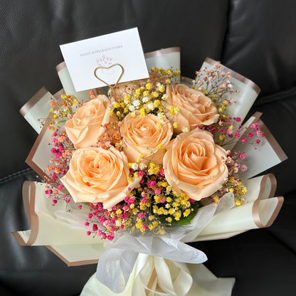 A bouquet of champagne Roses and rainbow Baby’s Breath presented on a dark background, with a complimentary message card included.