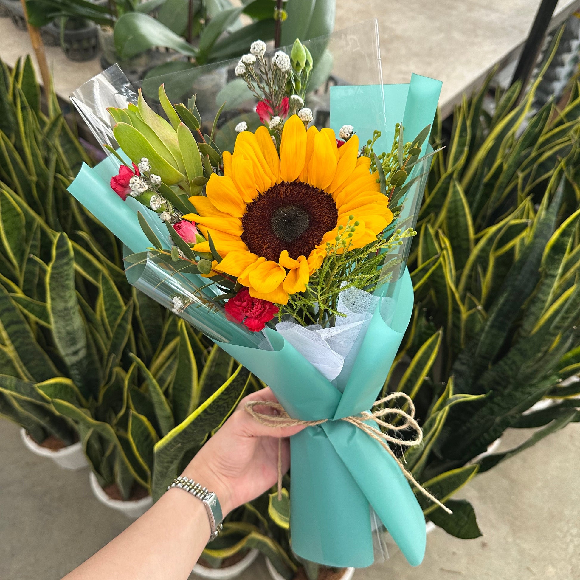 Bouquet of flowers with a sunflower held by a hand, with a blurred background