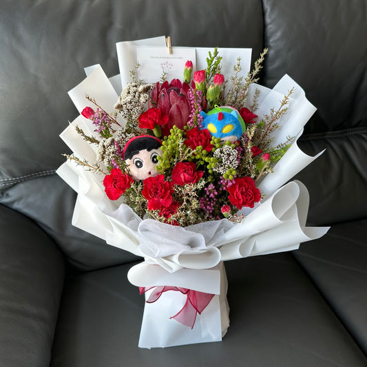 A bouquet of flowers with red carnations and other South African blooms, wrapped in white paper with lbbxx soft toy characters.