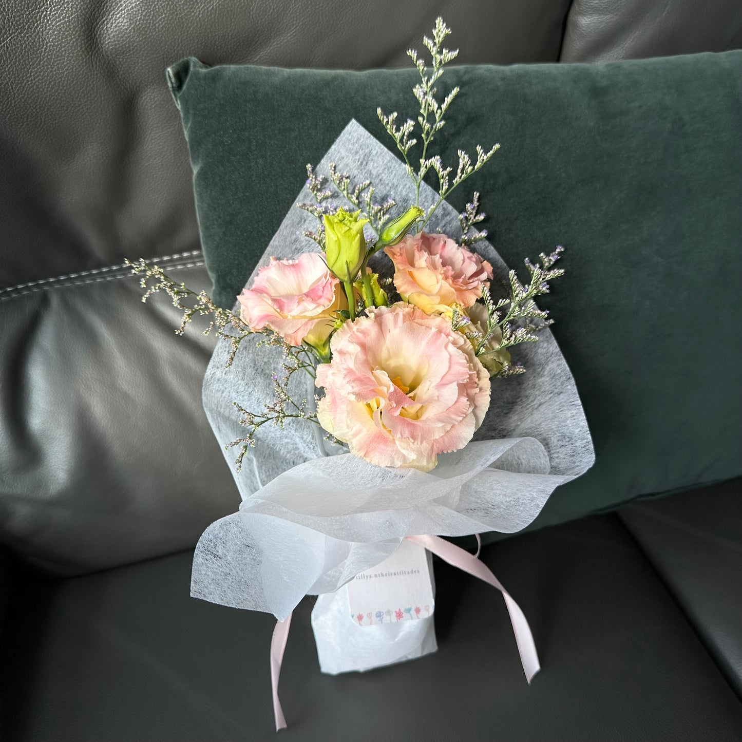 A bouquet of pink and white flowers wrapped in white paper, placed on a dark cushion.