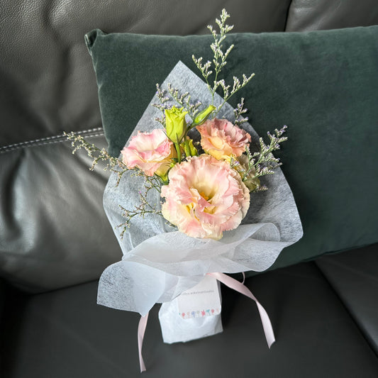 A bouquet of pink and white flowers wrapped in white paper, placed on a dark cushion.