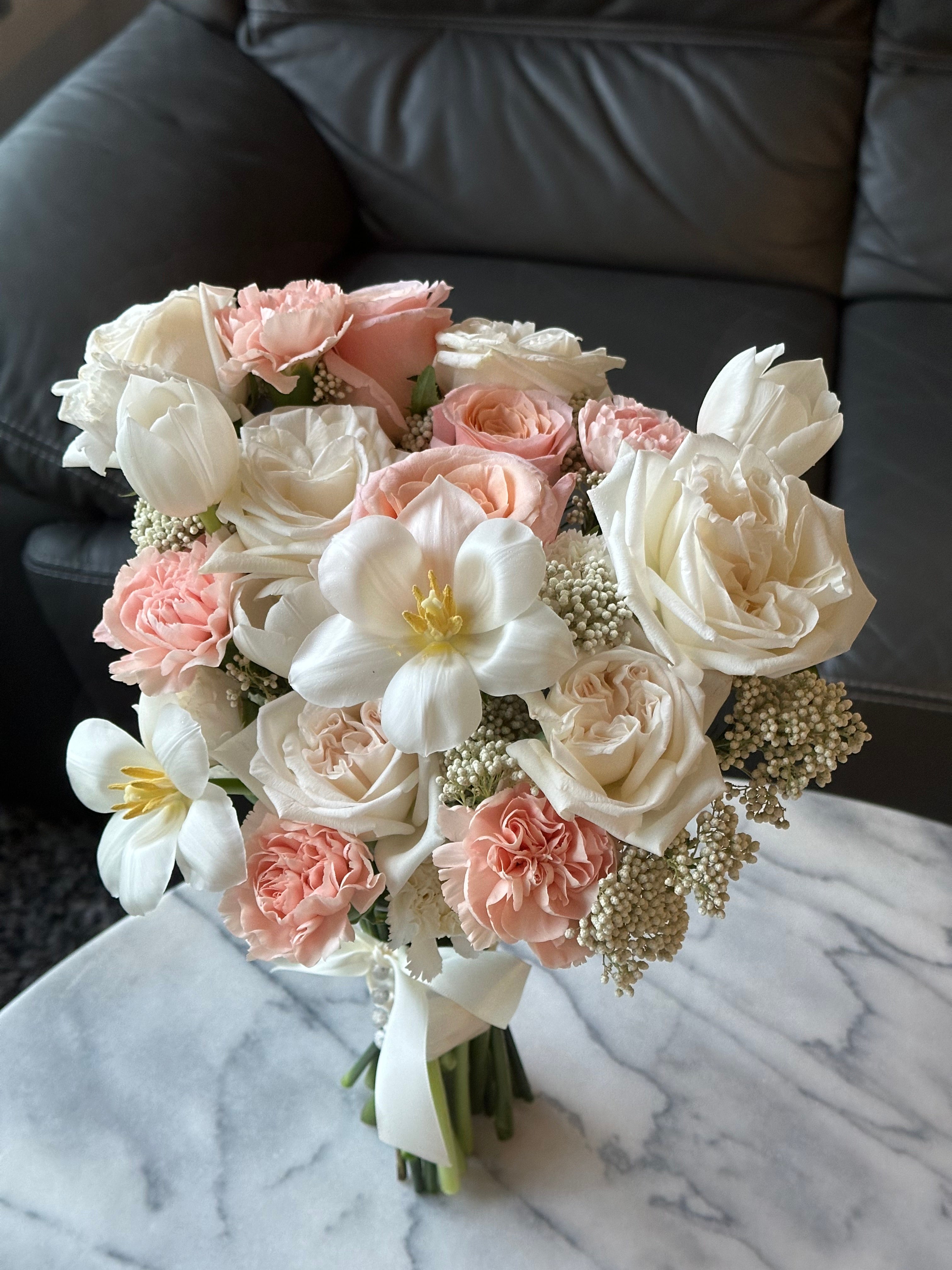 Bouquet of pink and white tulips and roses flowers on a marble surface with a gray couch.