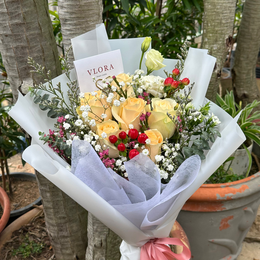 Bouquet of flowers with a pink ribbon and a card labeled 'Vlora' in an outdoor setting.