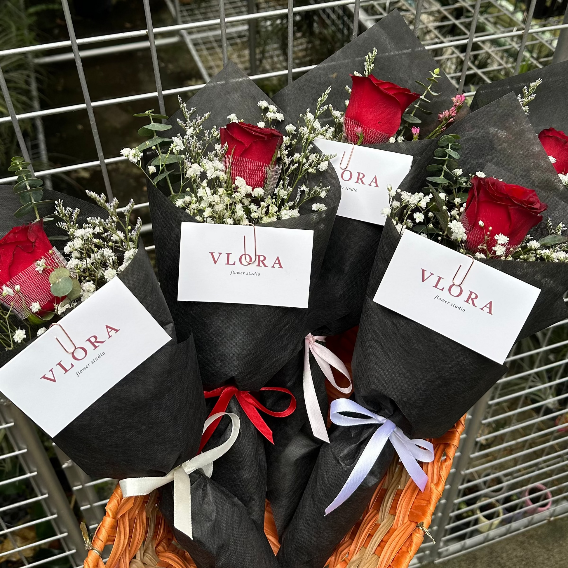 Bouquets of red rose flowers with black wrap and red roses on a woven mat, against a metal fence background.