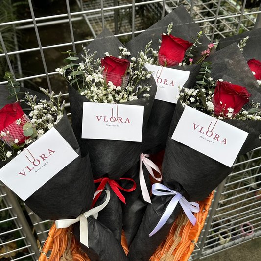 Bouquets of red rose flowers with black wrap and red roses on a woven mat, against a metal fence background.