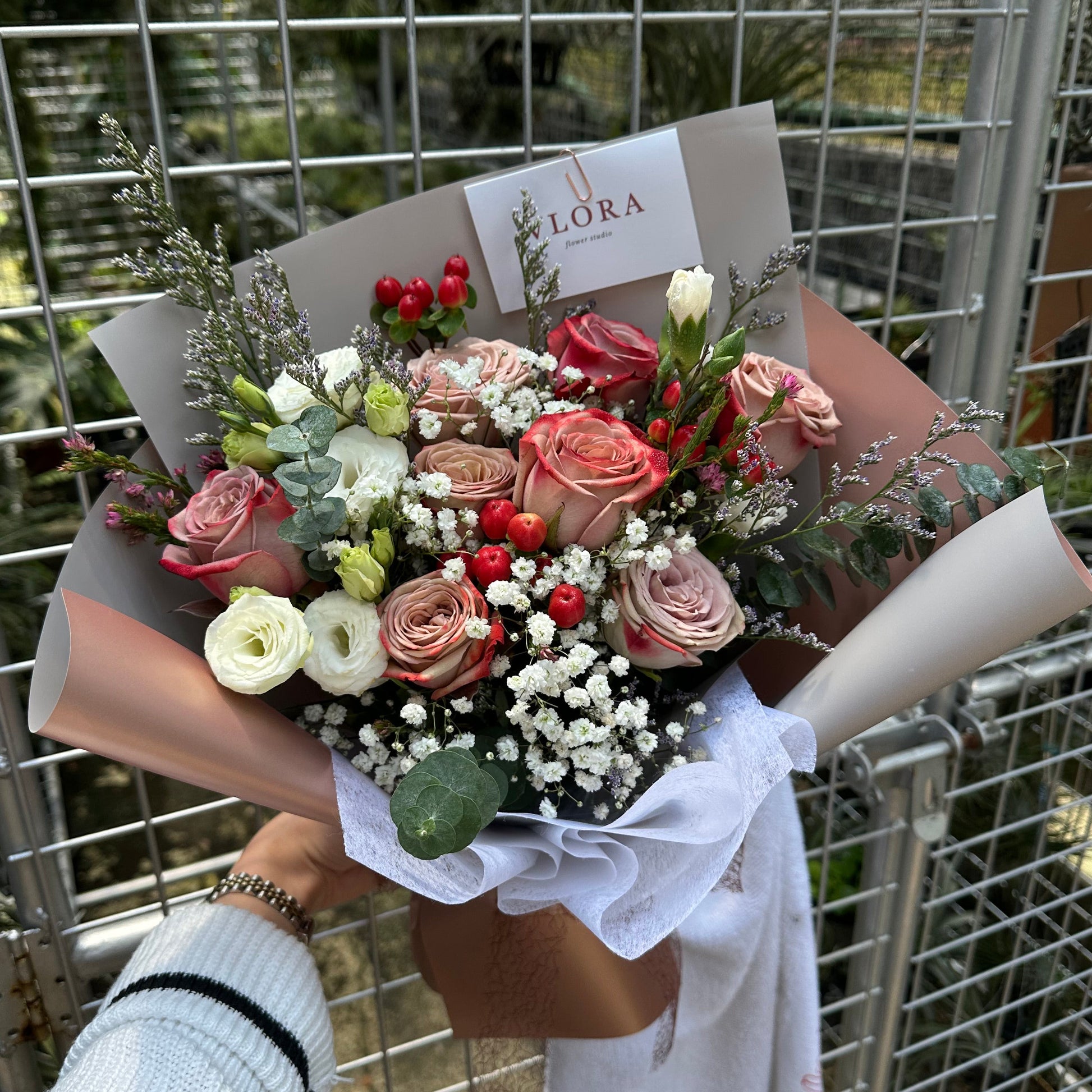 Bouquet of cappuccino roses flowers held by a person with a visible brand label, against a metal grid background.