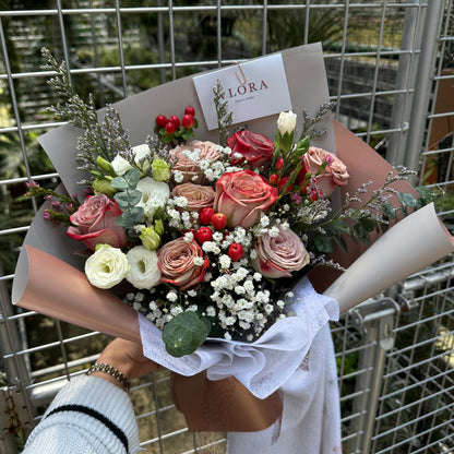 Bouquet of cappuccino roses flowers held by a person with a visible brand label, against a metal grid background.