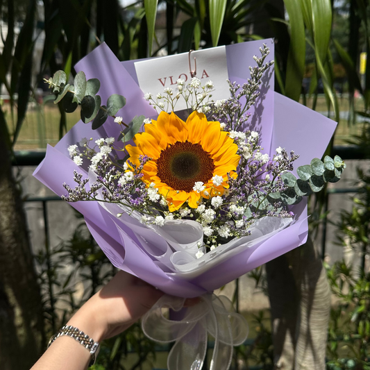 Bouquet with a sunflower and white baby's breath, wrapped in purple paper.