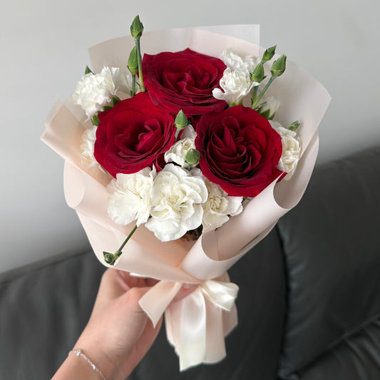 A bouquet of flowers consisting of red roses and white carnations, wrapped in white paper with a ribbon.