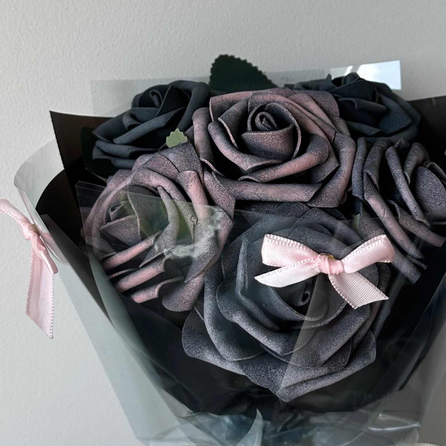 A bouquet of black foam roses with a tinge of pink, wrapped in black paper and adorned with pink ribbons.
