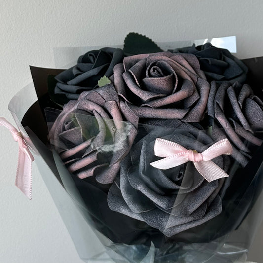 A bouquet of black foam roses with a tinge of pink, wrapped in black paper and adorned with pink ribbons.