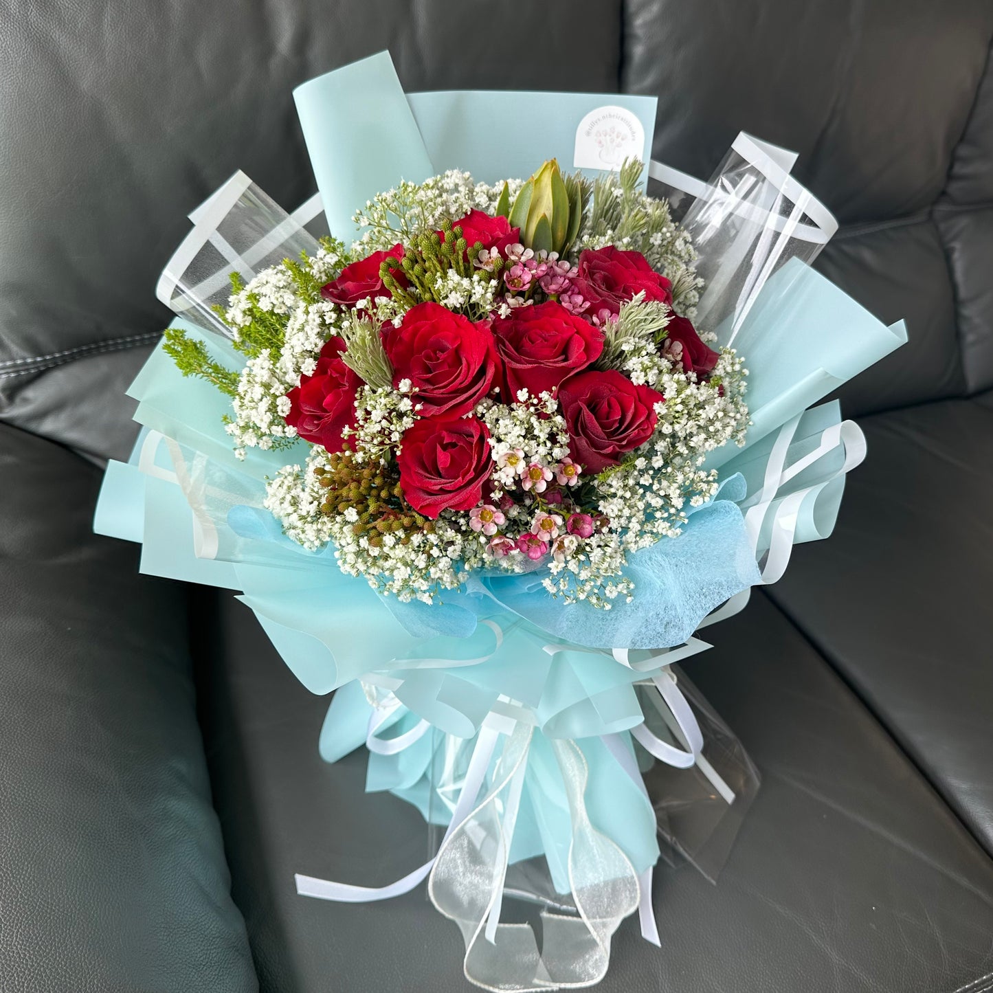 A bouquet of red roses wrapped in turquoise paper with baby's breath and accent flowers.