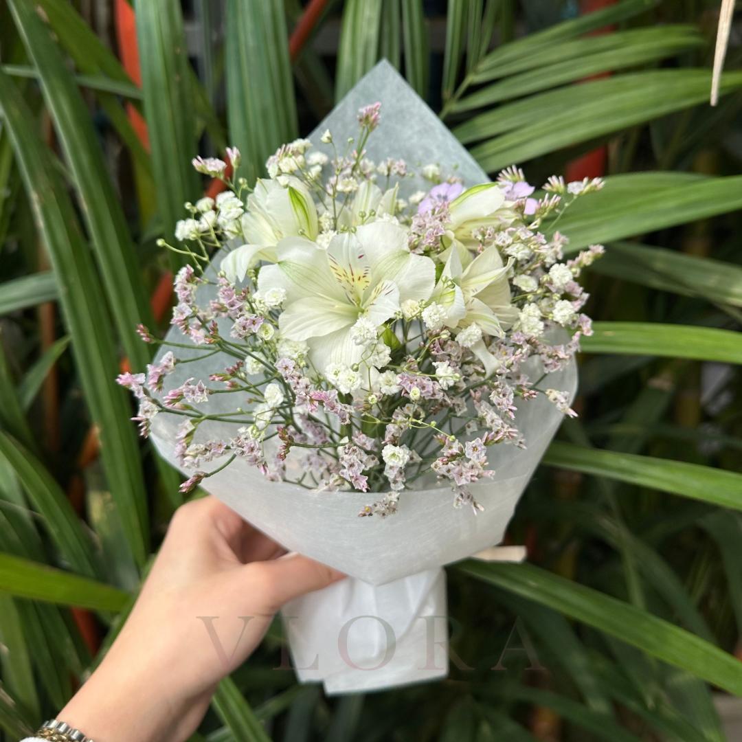 Bouquet of white flowers with small pink flowers held by a hand against a green leafy background
