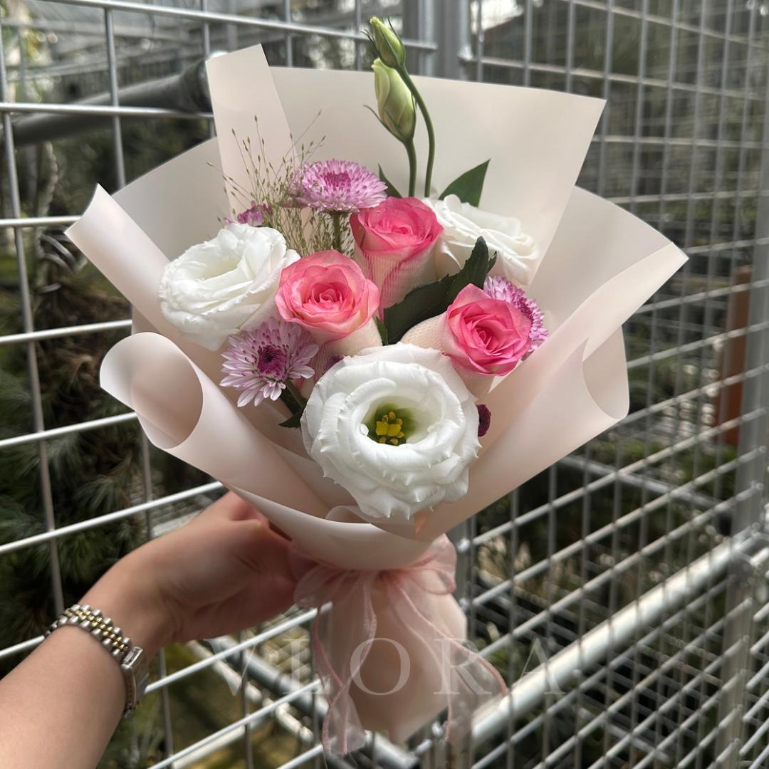 Bouquet of pink and white flowers held by a person with a metal fence background