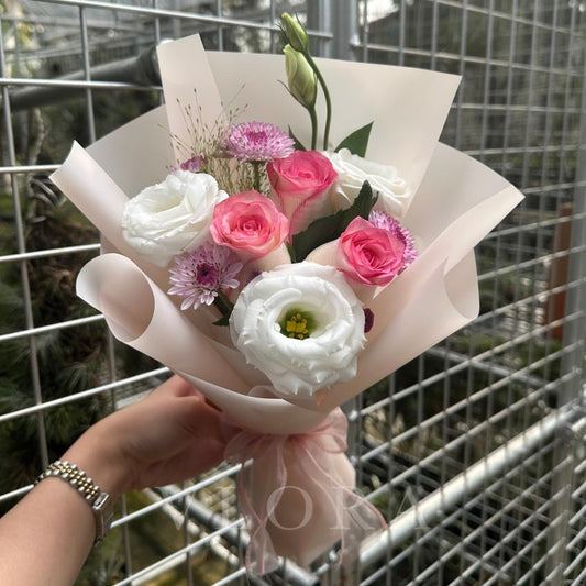 Bouquet of pink and white flowers held by a person with a metal fence background