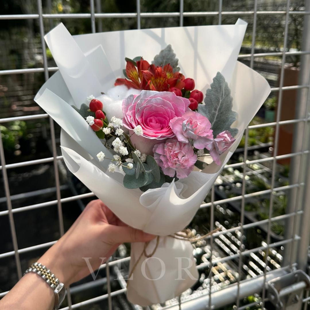 A pink rose sprayed silver, mixed flower bouquet wrapped in white.