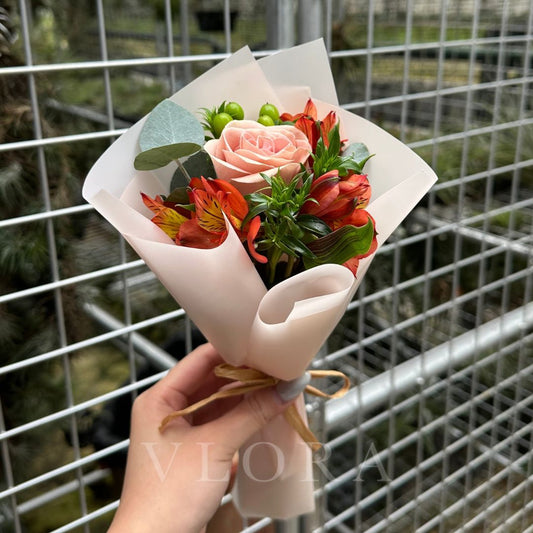 Bouquet of cappuccino rose flowers held by a hand with a metal fence background