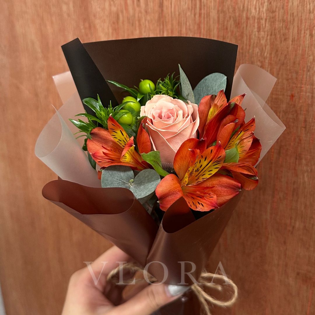 Bouquet of flowers wrapped in brown paper with a visible brand logo on a wooden surface.