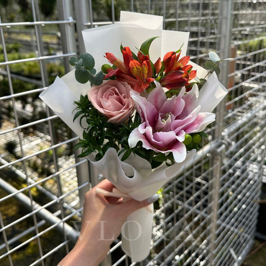 Bouquet of Rose-Lily, Cappuccino Rose, Hypericum Green, Red Alstroemeria, flowers held by a hand in front of a metal grid background