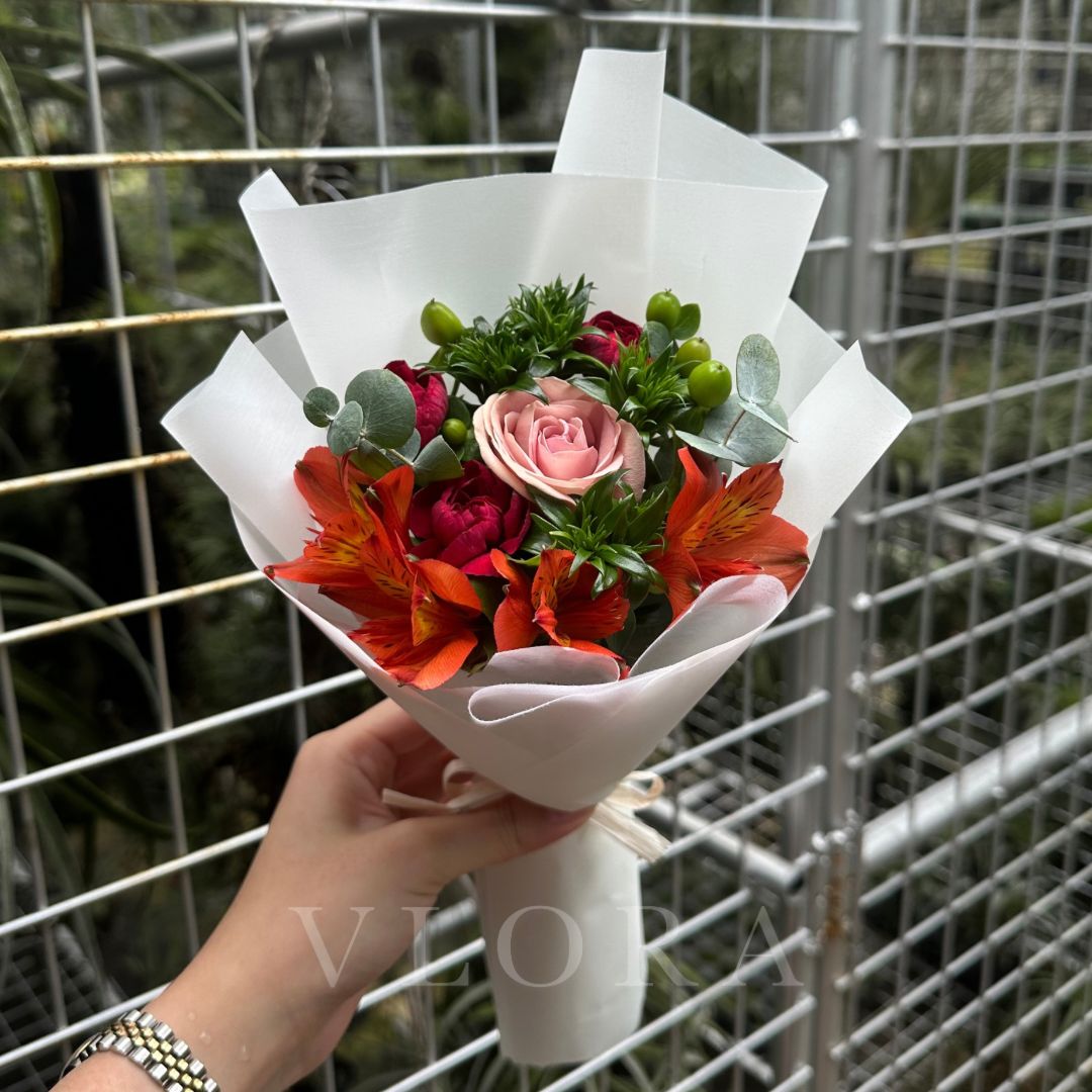 A fresh flower bouquet featuring a cappuccino rose, hypericum green, red carnations and red alstroemeria. wrapped in white.