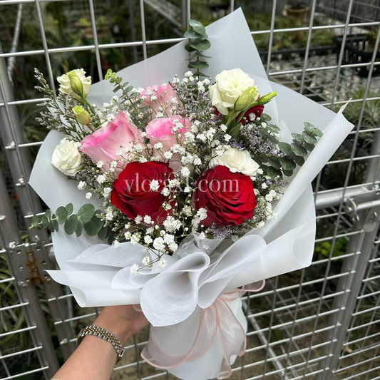 Bouquet of red and pink roses flowers held by a person in front of a wire fence