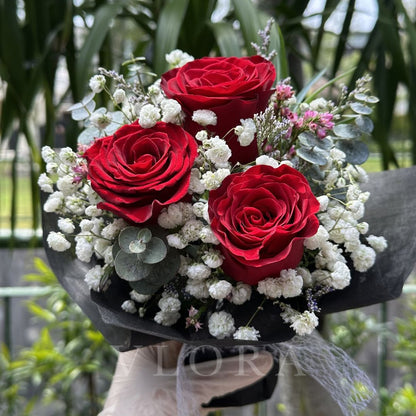 Bouquet of red roses with white flowers and greenery held by a person.