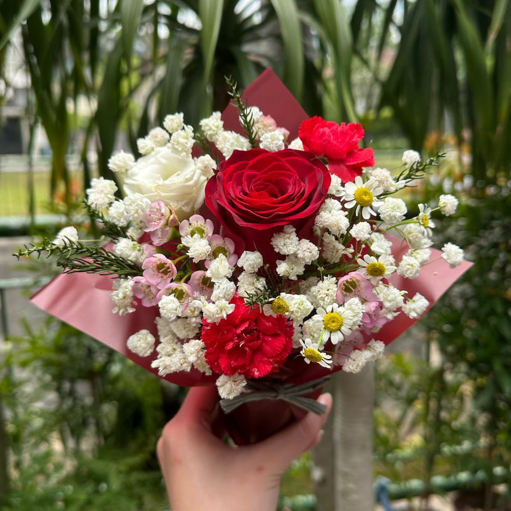 Bouquet of red roses and white flowers held in front of a green leafy background