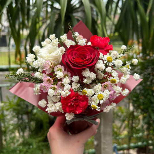 Bouquet of red roses and white flowers held in front of a green leafy background