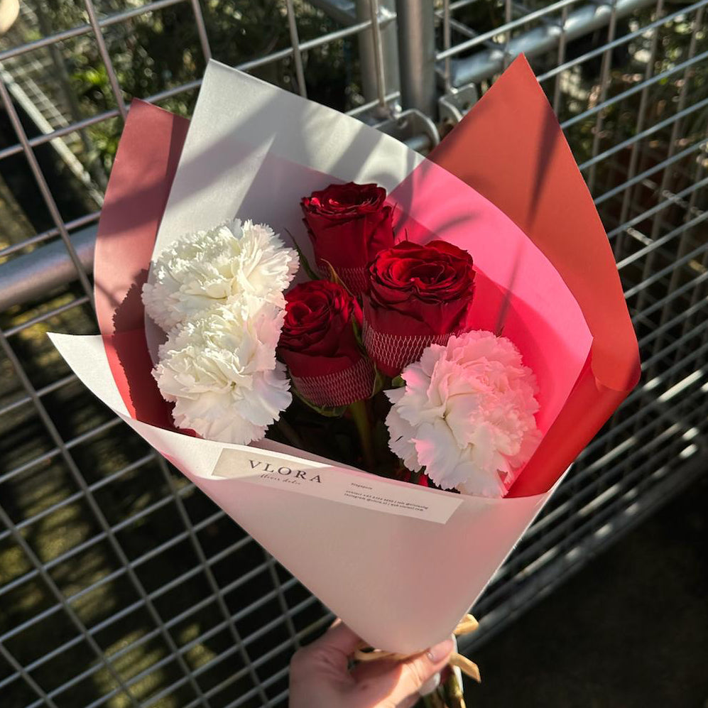 Bouquet of red and white flowers held in front of a metal fence.