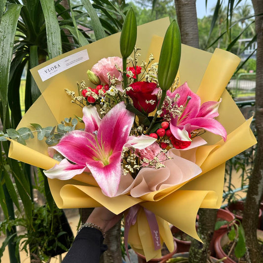 Bouquet of lily flowers with a yellow wrap held by a person, surrounded by potted plants.