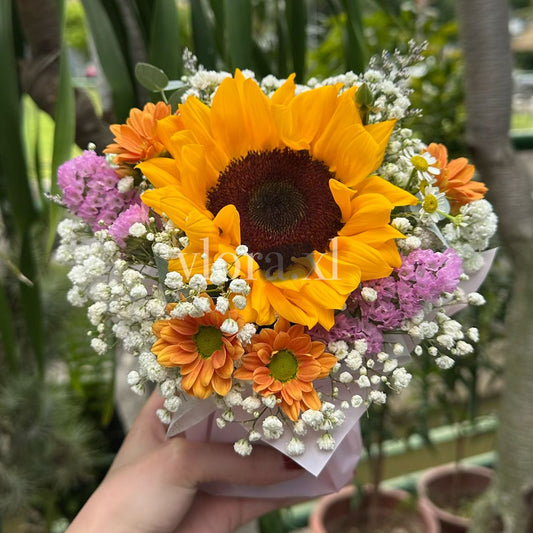 Hand holding a bouquet of sunflowers and other flowers in a garden setting