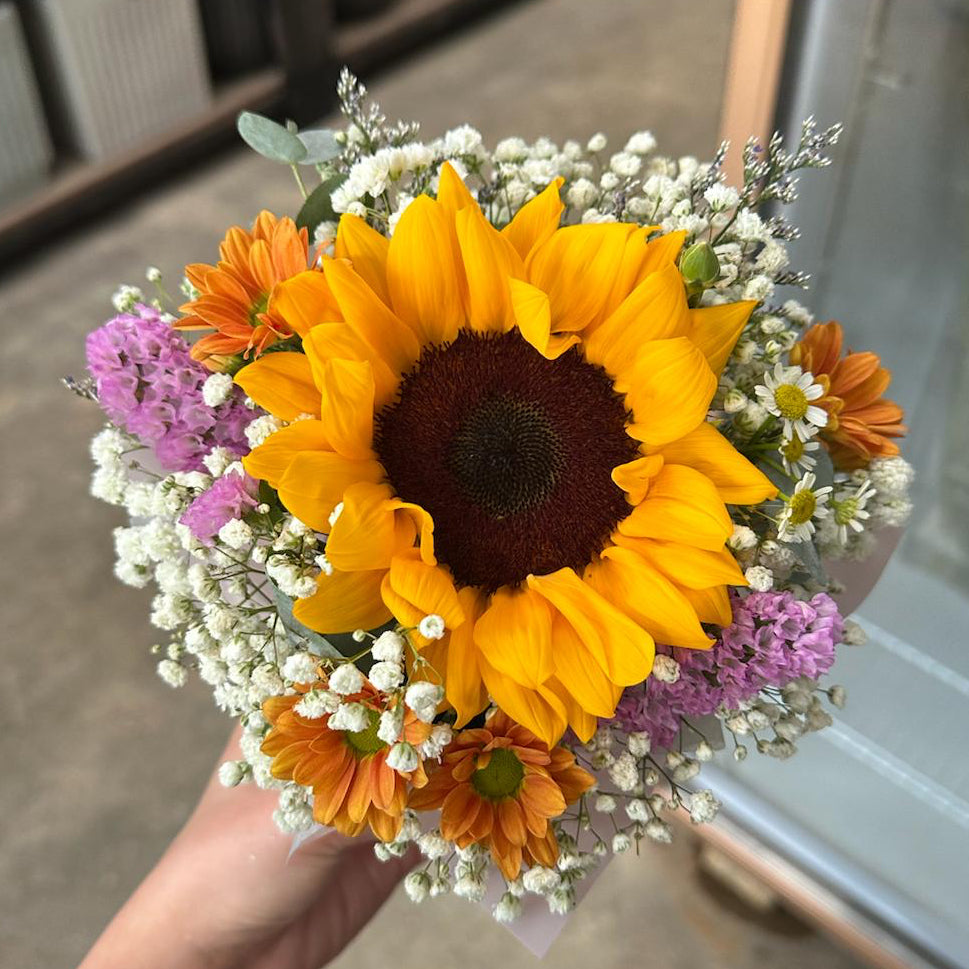 Bouquet of sunflowers and other flowers held by a person indoors.