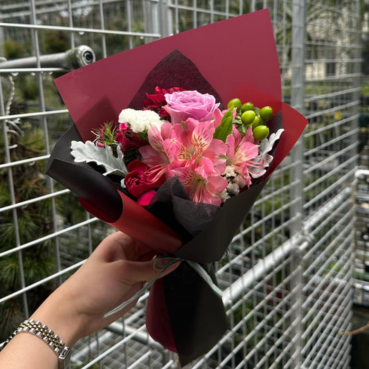 Bouquet of purple roses flowers held by a hand in front of a greenhouse.