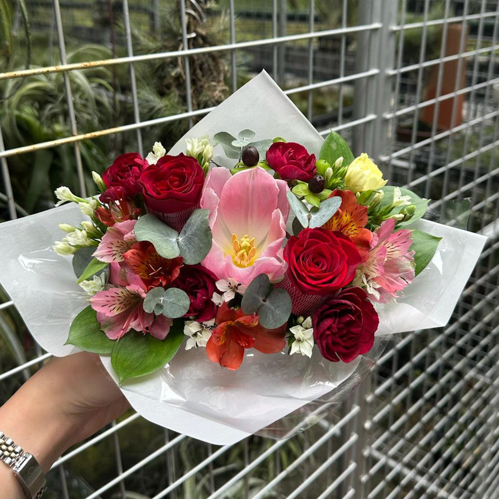 Bouquet of red roses and pink tulips flowers held by a person in front of a metal fence