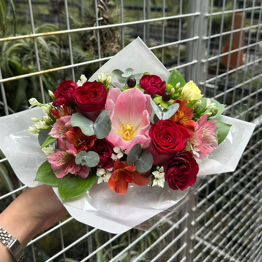 Bouquet of red roses and pink tulips flowers held by a person in front of a metal fence