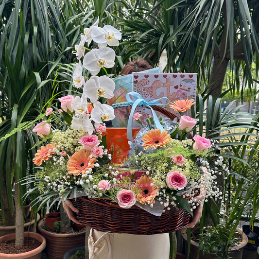 Person holding a floral basket with birds nest, a gift card, in a garden setting.