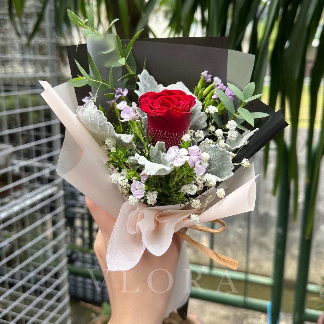Bouquet with a red rose held by a person, against a blurred green background
