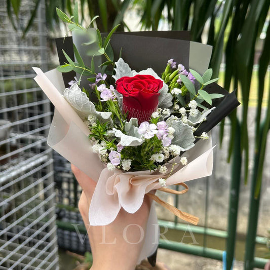 Bouquet with a red rose held by a person, against a blurred green background