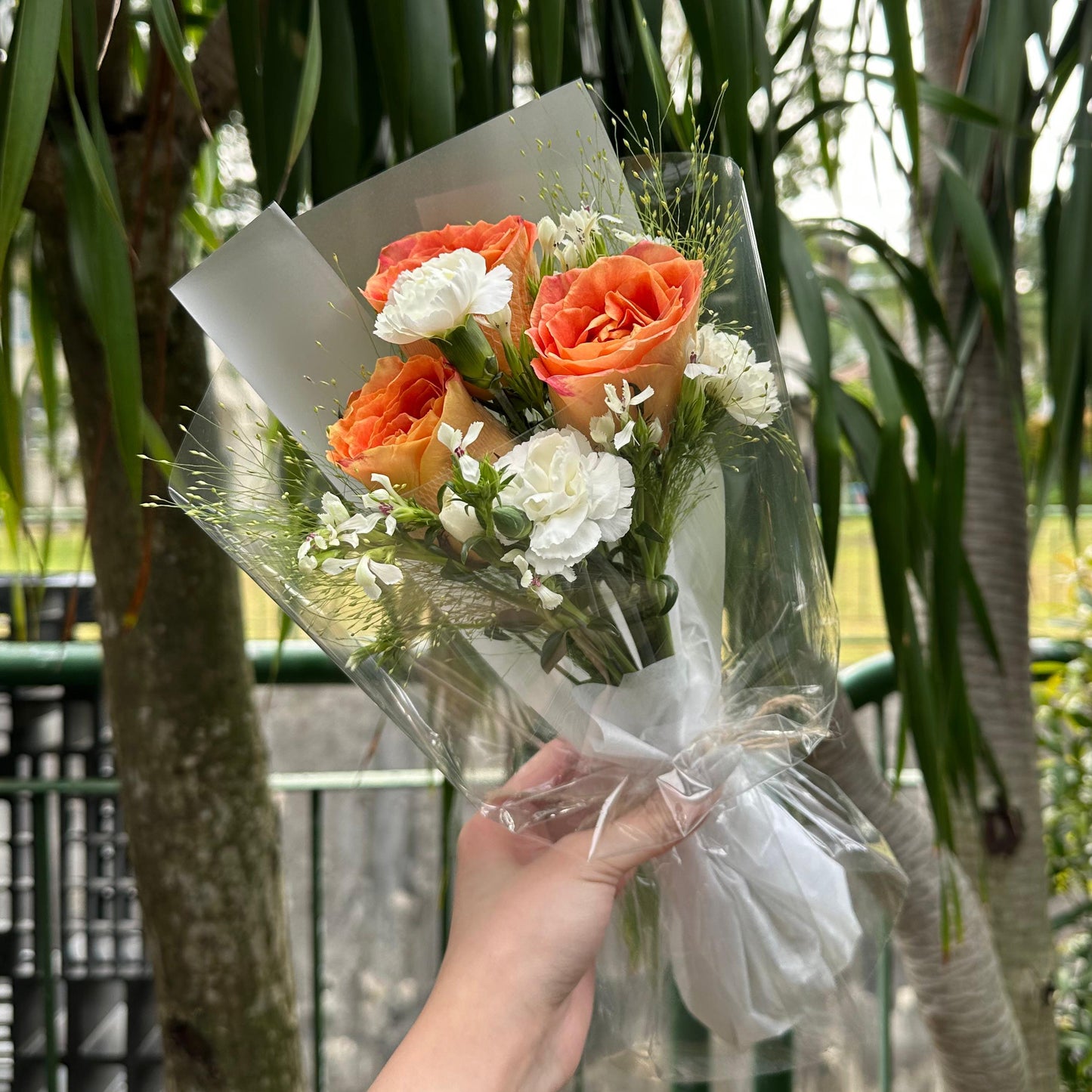 Bouquet of orange and white flowers held by a person with greenery in the background