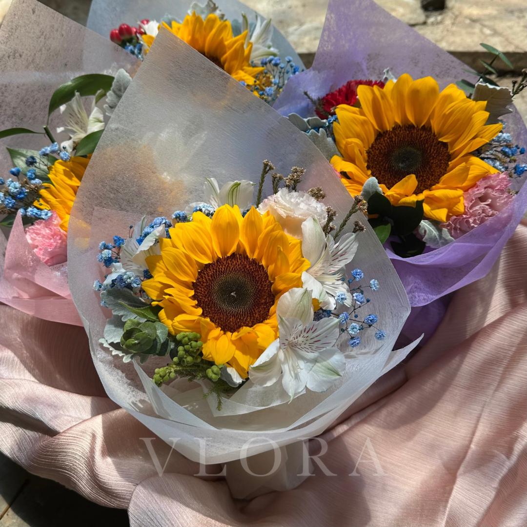 Bouquet of sunflowers and other flowers wrapped in paper with 'Viora' branding.