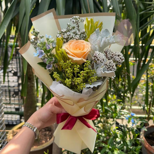 Bouquet of flowers with a red ribbon held by a hand in front of green plants.