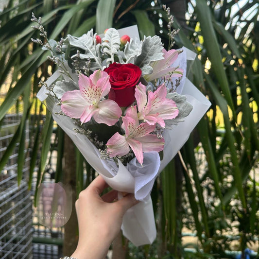 Bouquet of flowers with a red rose and pink lilies held by a hand against a blurred green background